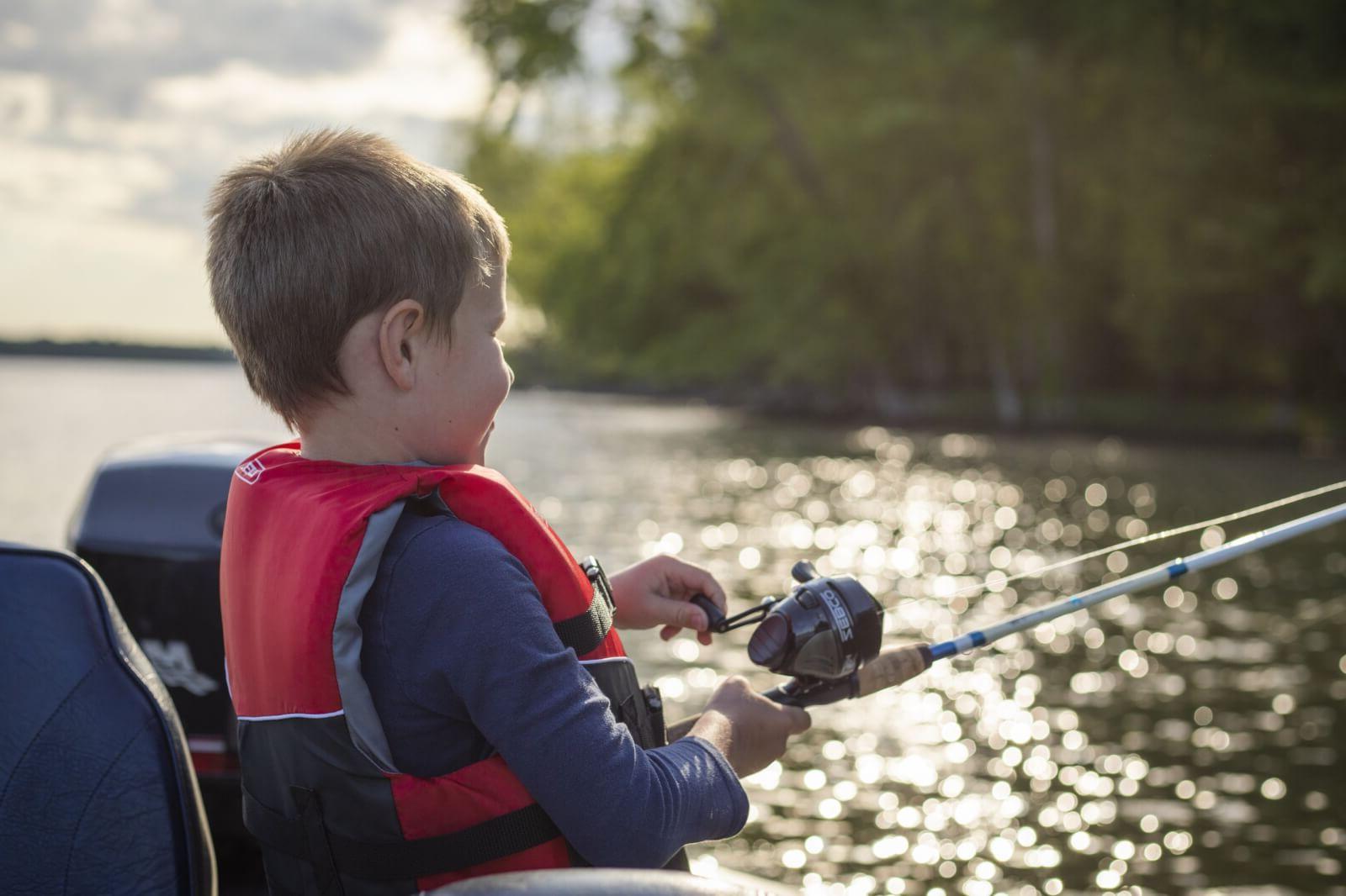一个穿着红色背心的小男孩，手里拿着一根钓竿，在湖面上划船